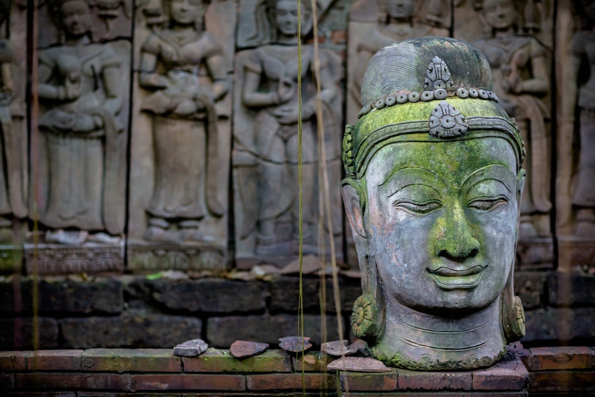 A terra cotta head of buddha sits in front of bas-relief in a terra cotta garden; Chiang Mai, Thailand